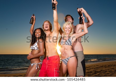 People (two couples) on the beach having a party, drinking and having a lot of fun in the sunset (people having bottles in their hands)