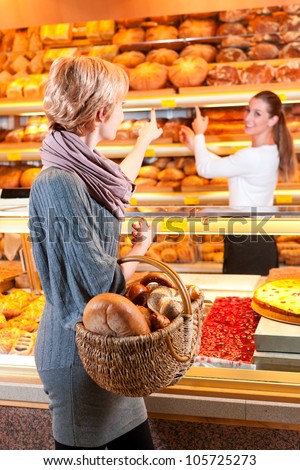 Female baker or saleswoman in her bakery with a female customer and fresh pastries or bakery products