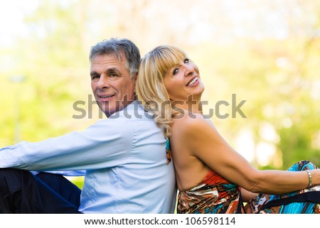 Mature or senior couple sitting on a meadow during spring in the city and enjoy the sun