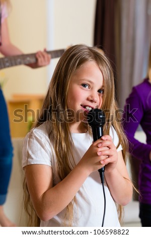 Children - three sisters - playing in a band making music, focus on girl with microphone in front