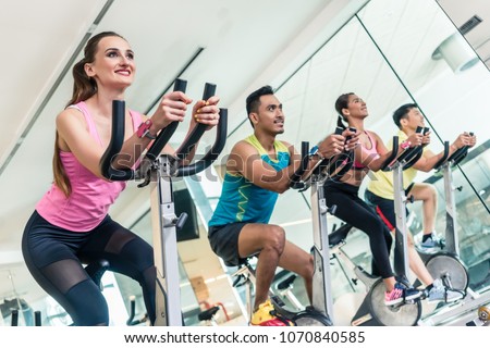 Side view of a beautiful fit young woman smiling while pedaling during cardio workout at indoor cycling group class in a modern fitness club