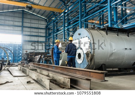 Experienced worker writing observations while checking the quality of manufactured industrial boilers