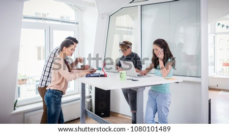 Busy co-workers using mobile technology connected to WI-FI network while sharing a desk in a modern work hub for freelancers and nomad entrepreneurs