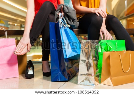 Two female friends with shopping bags having fun while shopping in a mall, the feet hurt already