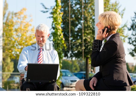 Business people working outdoors - he is working with laptop, she is calling someone on phone