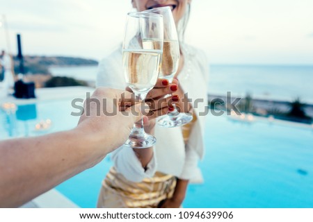 Woman and man clinking glasses at elegant pool party in summer