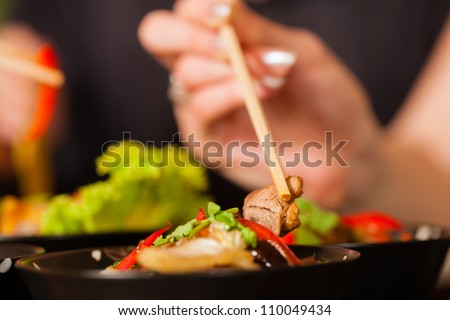 Young people eating in a Thai restaurant, they eating with chopsticks, close-up on hands and food