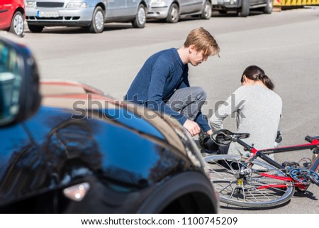 Helpful young man giving first aid to an injured young woman after suffering a painful strain or fracture in bicycle accident on the street