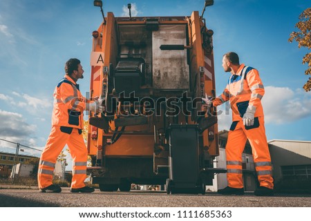 Two refuse collection workers loading garbage into waste truck emptying containers