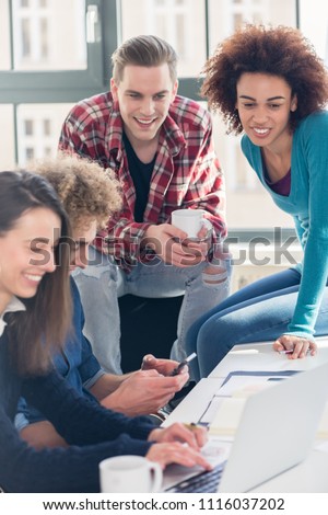 Two millennial students watching together an online funny video on laptop while sitting at desk during break in a modern college or university