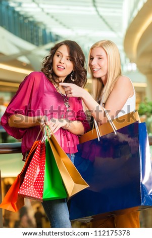Two female friends with shopping bags having fun while shopping in a mall