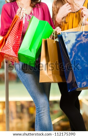 Two female friends with shopping bags having fun while shopping in a mall, close-up on bags