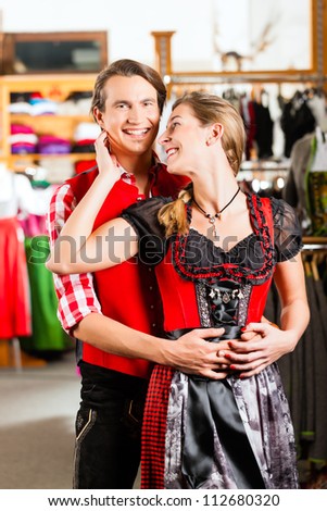 Traditional clothes - young couple is buying Tracht - a dirndl and a lederhosen in a shop, they do try it on before