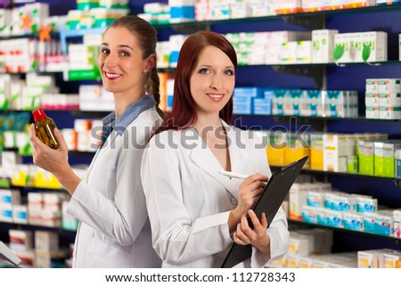 Pharmacist with female assistant in pharmacy standing in front of shelf with drugs