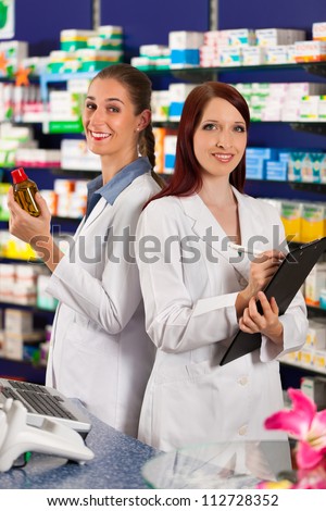 Pharmacist with female assistant in pharmacy standing in front of shelf with drugs