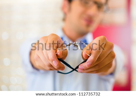 Young man at optician with glasses, he might be customer or salesperson, focus on hands