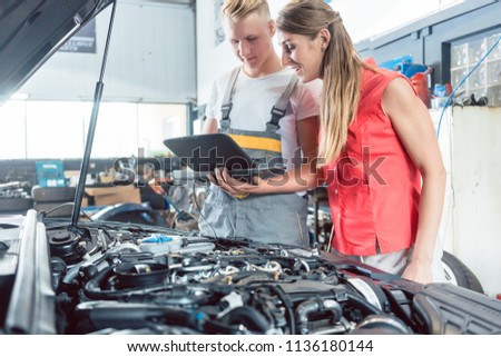 Reliable auto mechanic showing to a female customer the engine error codes scanned by a car diagnostic software in a modern automobile repair shop