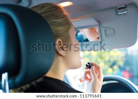 Young woman with lipstick in car looks into review mirror