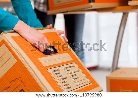 Young woman - presumably friends - with moving box in her house moving in or out of a apartment, focus on moving box