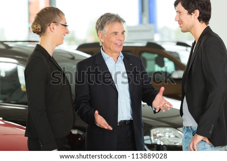 Mature single man with autos in light car dealership with a young couple, he obviously is buying a car or is a car dealer