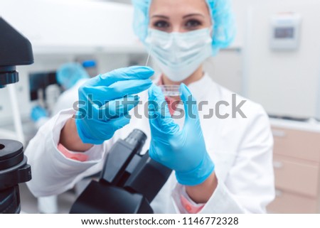 Scientist in laboratory showing petri dish with fertilized egg cell in her hand