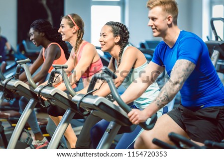 brunette beautiful woman smiling while cycling on a modern fitness bicycle during group spinning class at the gym