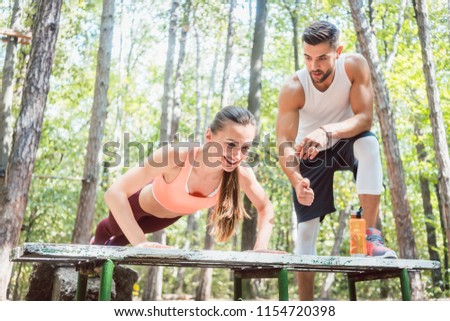 Sporty woman doing push-up in an outdoor gym, her boyfriend is watching her