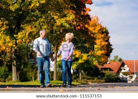 Man and woman, senior couple, having a walk in autumn or fall outdoors, the trees show colorful foliage