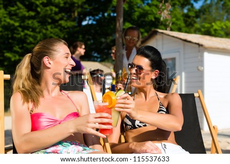 People at beach drinking having a party, two girls clinking glasses with cocktails having fun