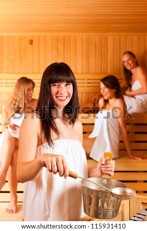 Wellness - young happy women in sauna of a Spa, water and scent are splashed on hot stones for steam
