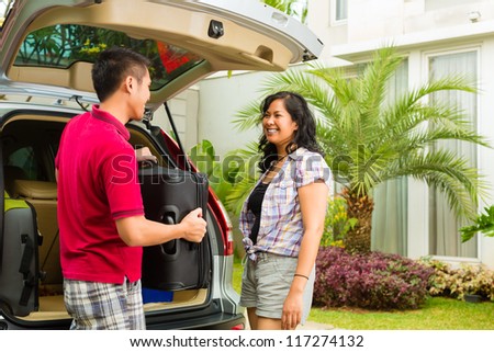 Asian couple packing car with suitcases for holiday and smiling