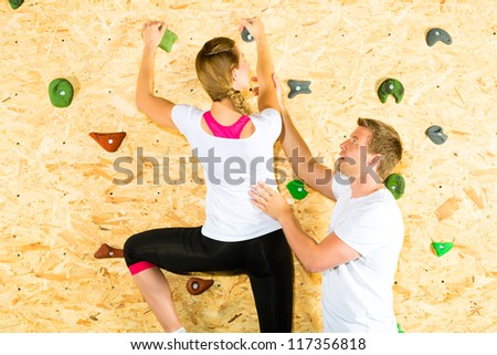 Woman and man climbing at climbing wall and training the body