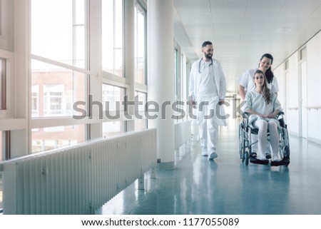 Doctor, nurse, and patient in wheelchair walking on hospital corridor