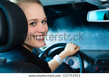 Young woman drives car in wash station cleaning the auto