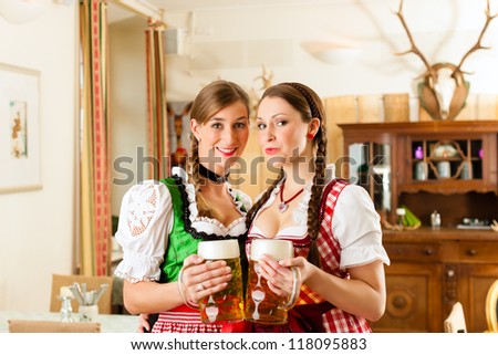 Two young women in traditional Bavarian Tracht in restaurant or pub with beer and beer stein