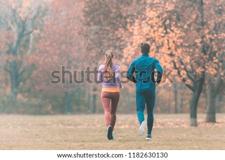 Fall running in a park, seen from behind couple of man and woman
