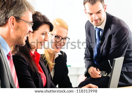 Four professionals in office in business attire looking at laptop screen working together