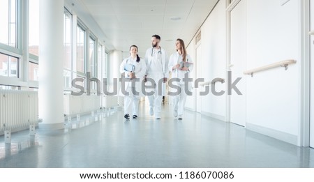 Doctors, two women and a man, in hospital walking down the corridor