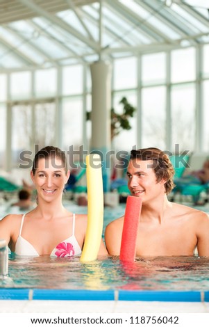 Fitness - a young couple - man and woman - doing sports and gymnastics or water aerobics under water in swimming pool or spa with swim noodle