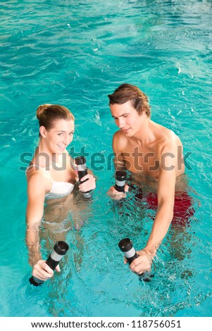 Fitness - a young couple - man and woman - doing sports and gymnastics or water aerobics under water in swimming pool or spa with dumbbells