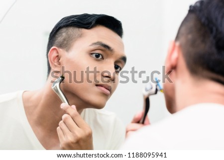 Close-up of young man shaving while looking in mirror