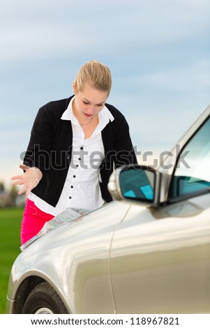 Young woman in front of bonnet of a car with map looking for directions, she is lost