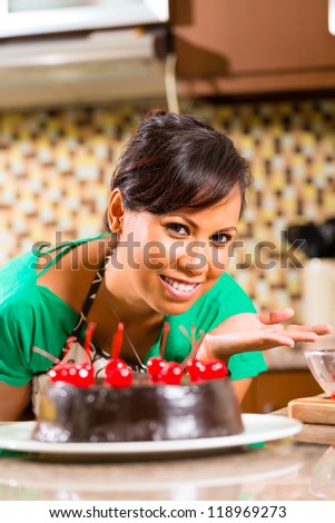 Asian woman presenting homemade chocolate cake with cherries she baked in her kitchen for dessert
