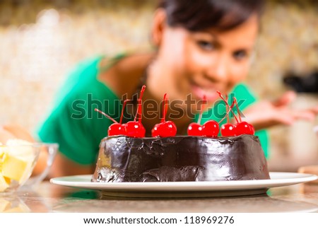 Asian woman presenting homemade chocolate cake with cherries she baked in her kitchen for dessert