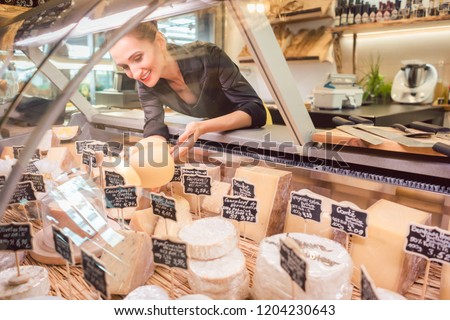 Shop clerk woman sorting cheese in the supermarket display to sell it