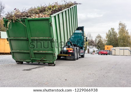 Truck loading container with waste green at recycling center to transport it away