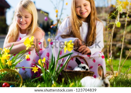 Children on an Easter Egg hunt on a meadow in spring, a living Easter Bunny is sitting in the Easter basket