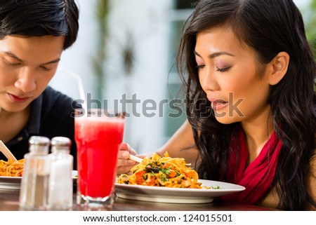 Asian man and woman in restaurant eating their food with chopsticks
