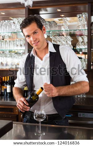 Barman standing behind the bar In restaurant opening a wine bottle
