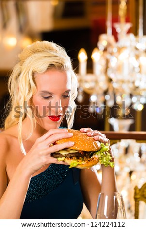 Young woman in a fine dining restaurant eat a hamburger, she behaves improperly